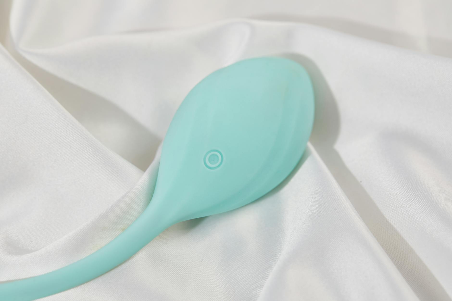 A stylish teal vibrator on smooth white silk fabric, representing careful care for sensitive intimate areas.
