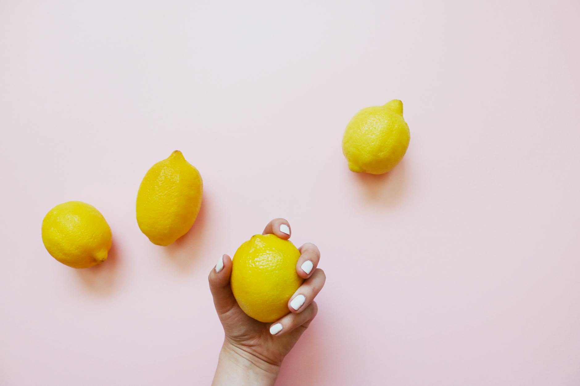 Une main tenant un citron frais sur fond rose doux, entourée de trois citrons supplémentaires.