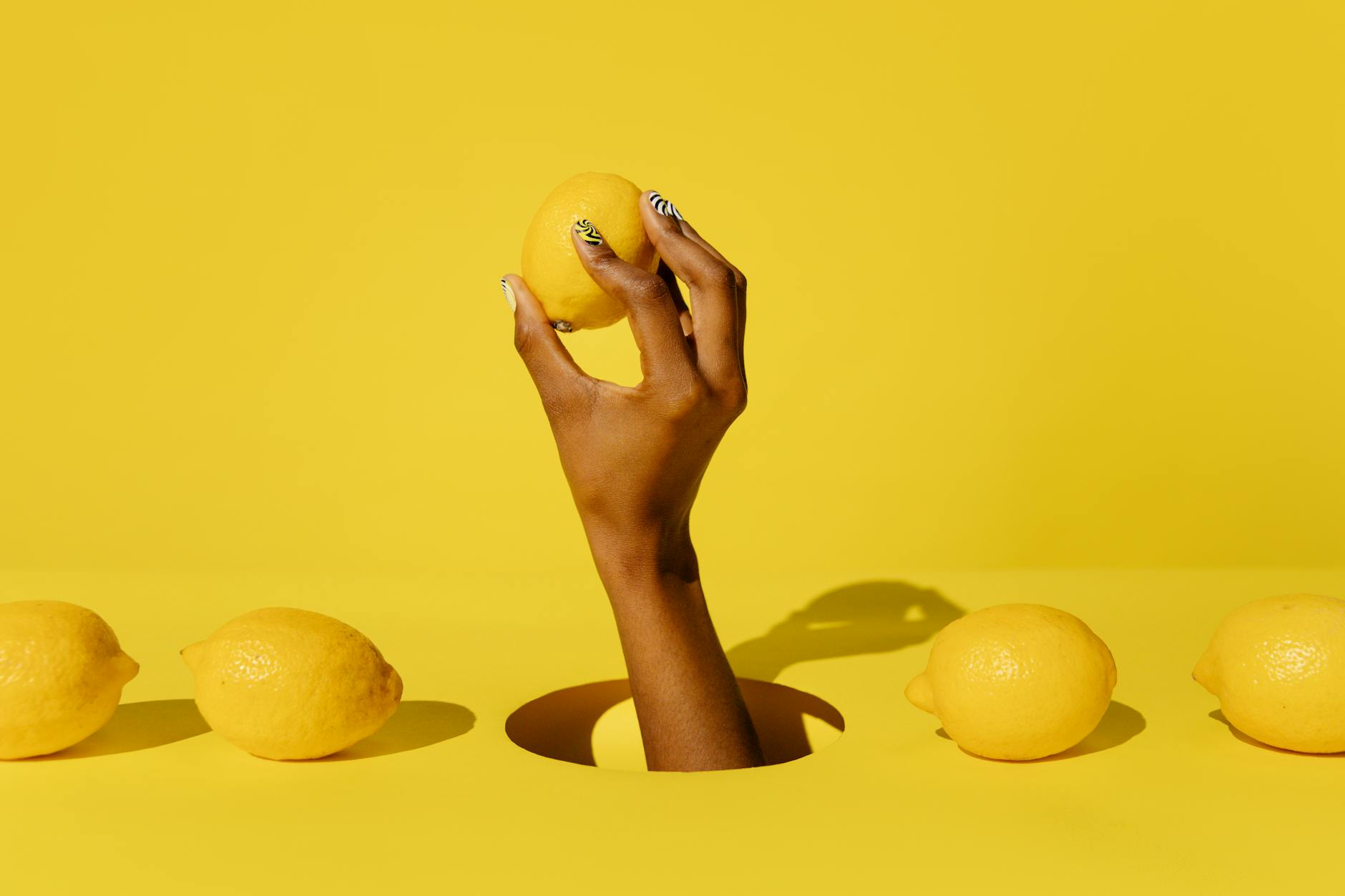 Une main tenant un citron frais contre un fond jaune vif, symbolisant la sensibilité renouvelée du clitoris.