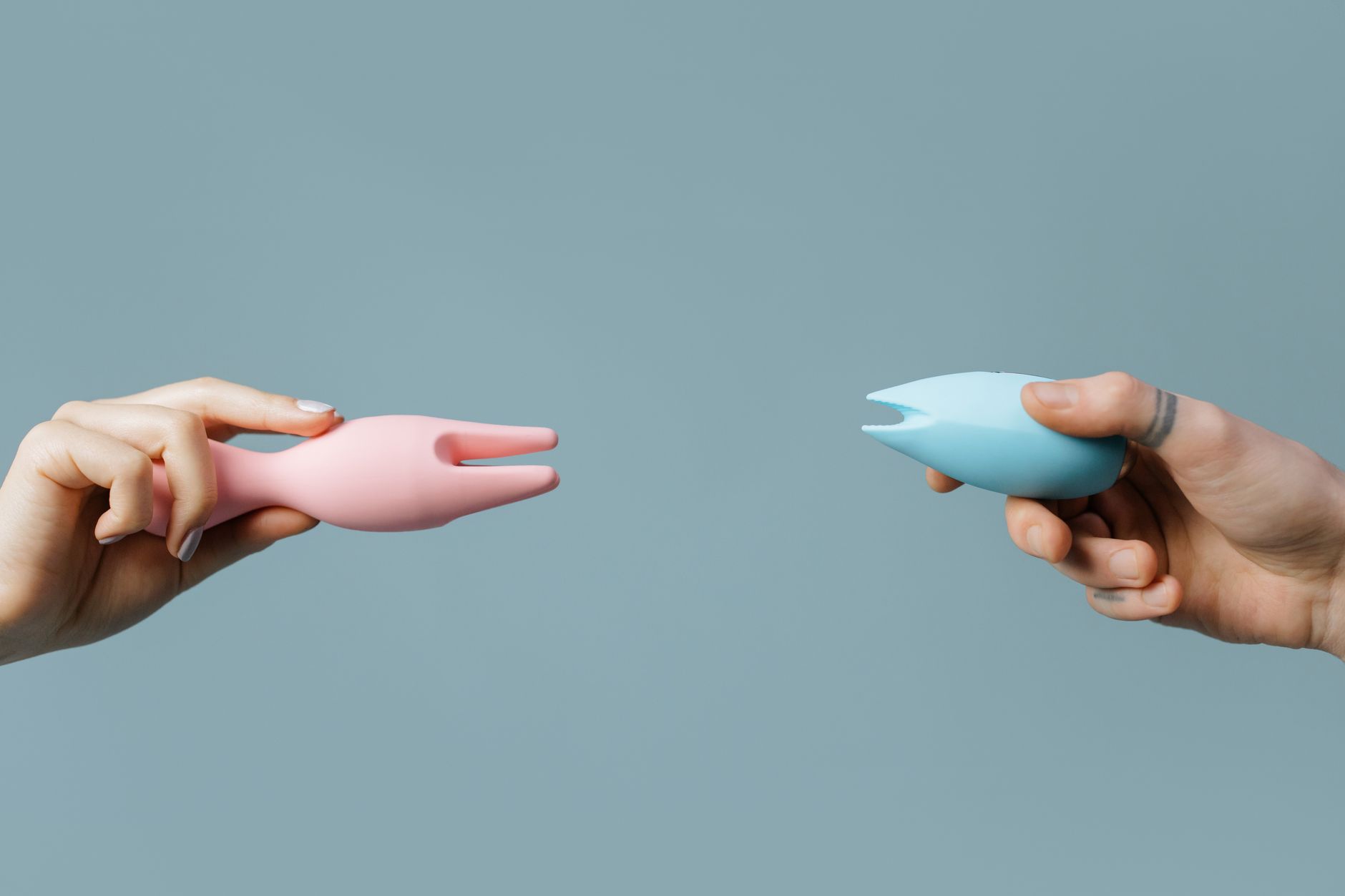 Two hands holding colorful vibrators against a soft pastel background