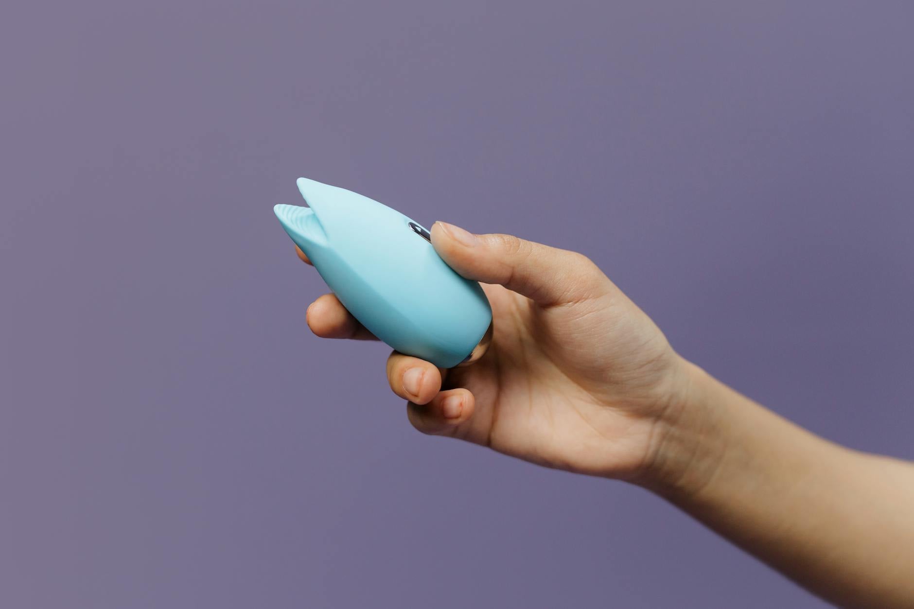 A person holding a blue silicone lemon vibrator against a purple background, representing personal pleasure and self-care