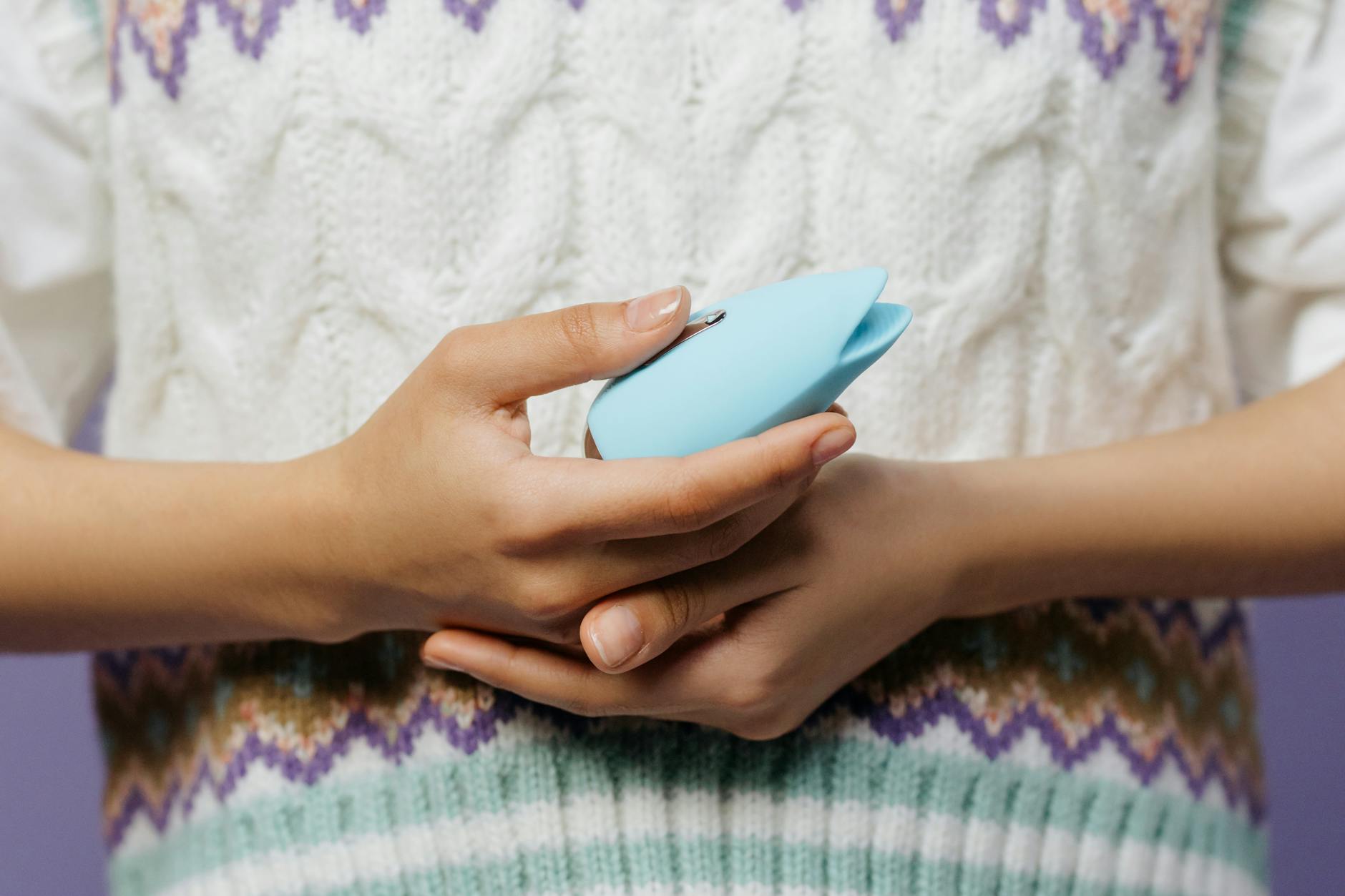 Close-up of hands holding a blue clitoral vibrator, representing personal pleasure and intimacy.