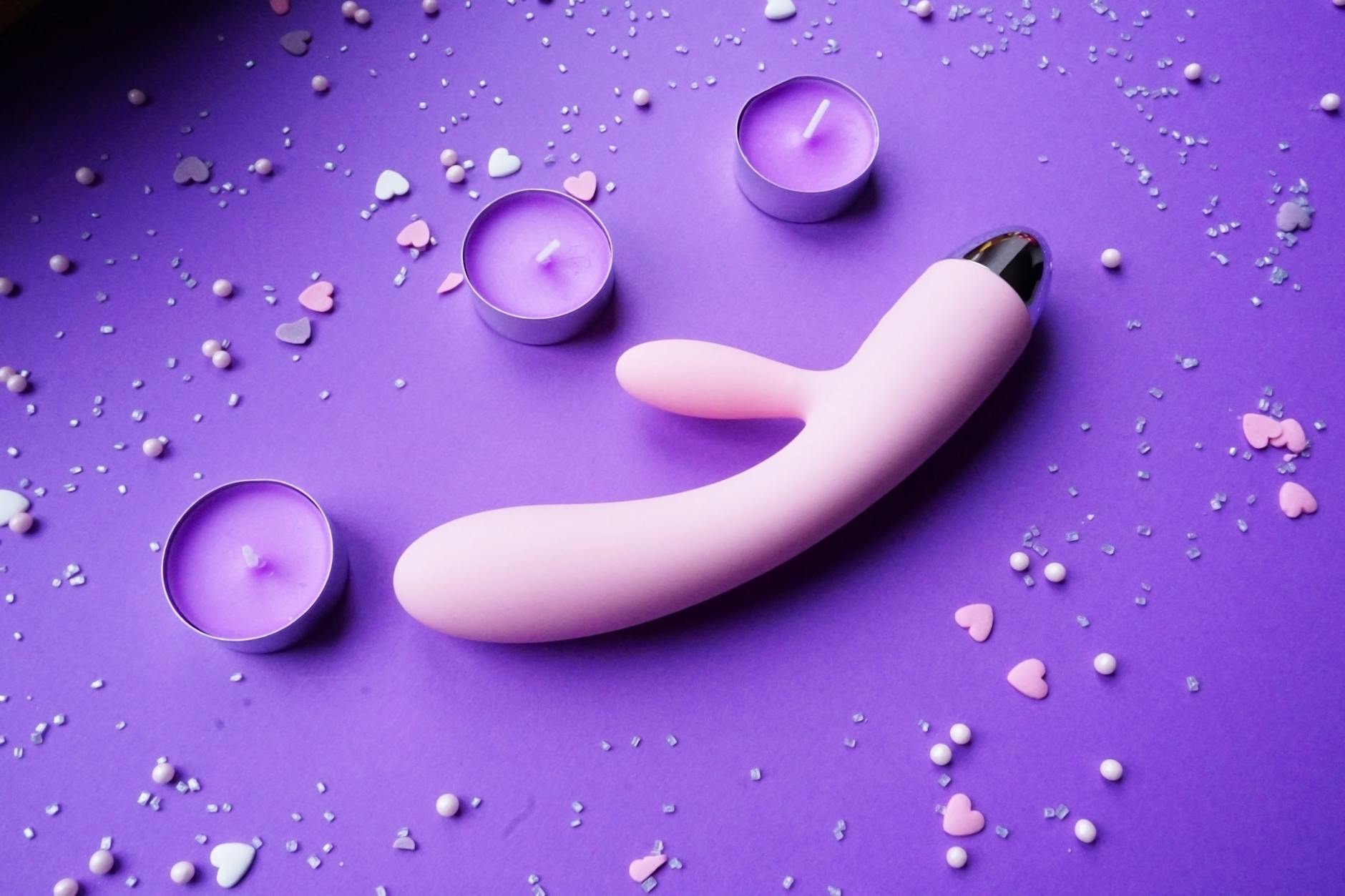 Pink vibrator on a purple background with heart confetti and candles for a romantic vibe.