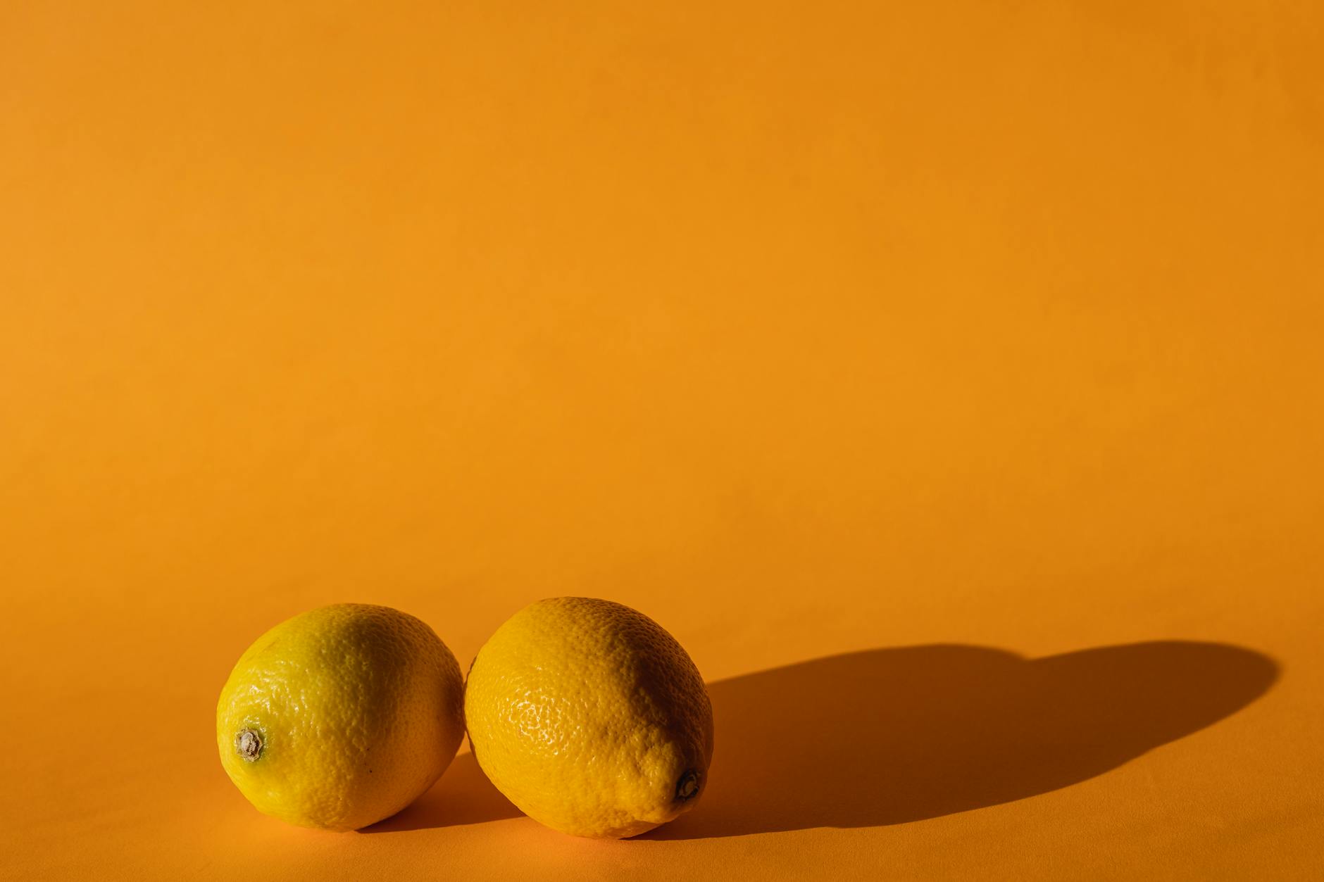 A hand holding a fresh lemon on soft pink background, representing citrus-shaped intimate wellness